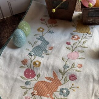 Camino de mesa con conejos, zanahorias, huevos bordados y motas azules en las orillas